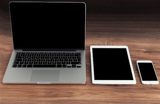 Apple Macbook, IPad and IPhone lined up next to each other on a wooden table.
