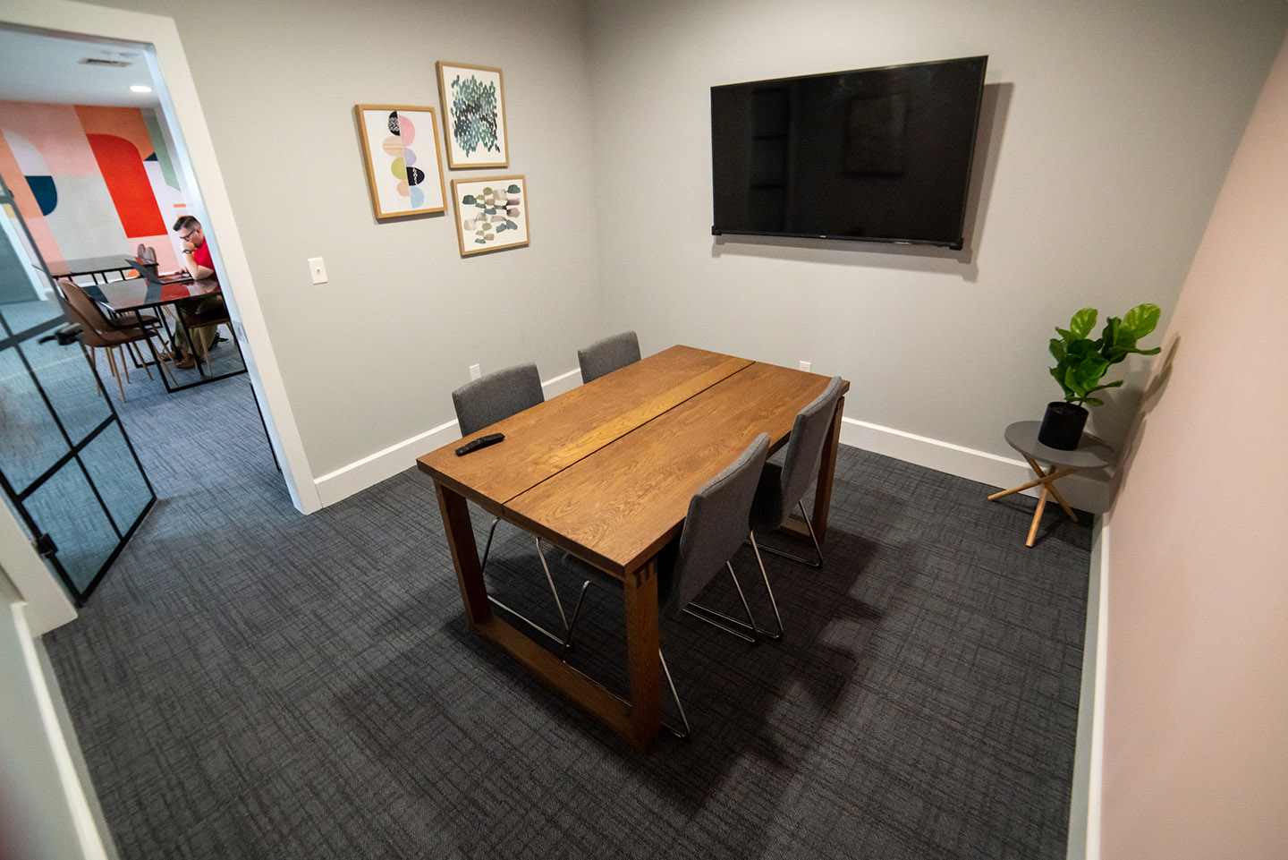 Office space feating a wooden table, four chairs, potted plans, wall art and a mounted tv