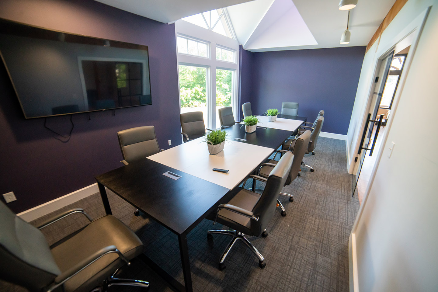 Moody conference room at Rebel HQ featuring long black and white table, purple walls and a mounted tv